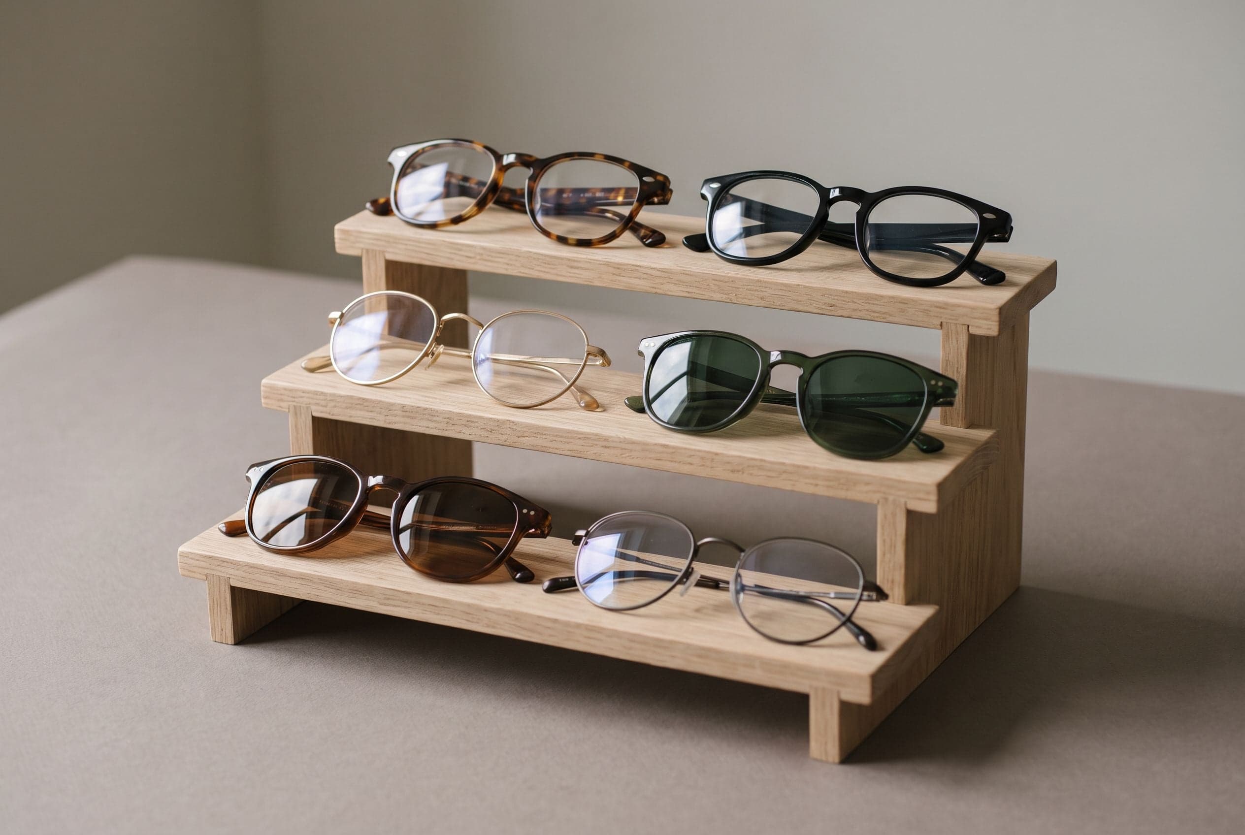 Glasses frames and sunglasses in tortoiseshell, black acetate and thin gold metal on a tiered oak display