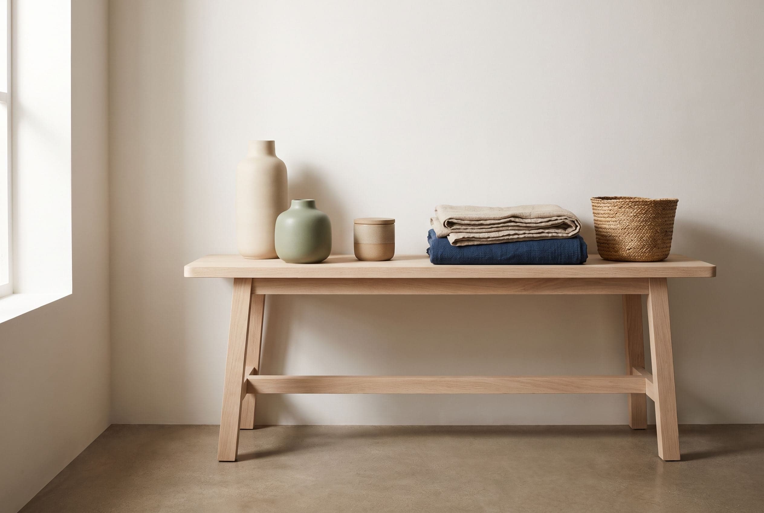 Vasi in ceramica, una candela con coperchio, plaid di lino piegati e un cesto intrecciato su una panca di rovere